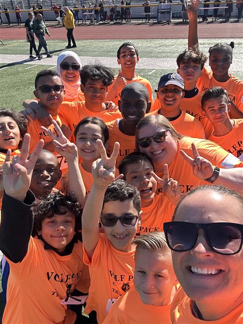 LArge group of students and school staff posing for photo in orange t-shirts.